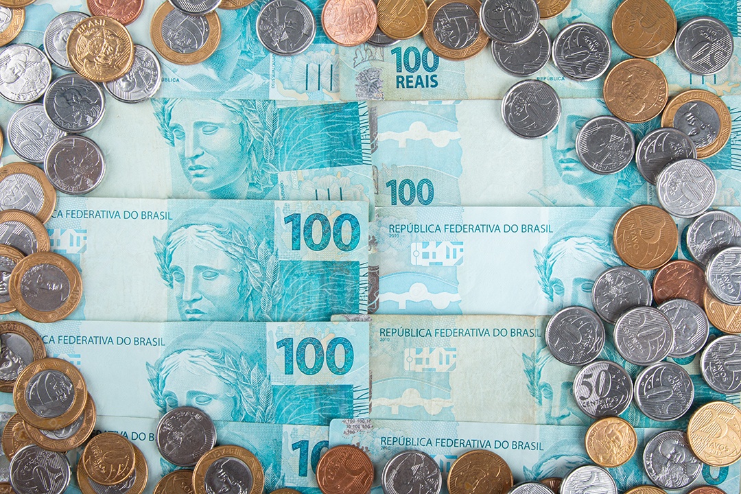 Dinheiro brasileiro com moedas espalhadas sobre notas de 100 reais