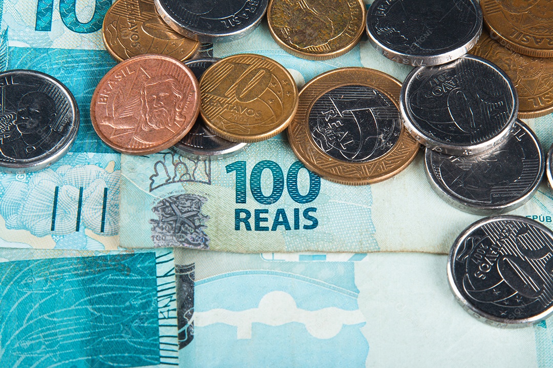 Dinheiro brasileiro com moedas espalhadas sobre notas de 100 reais