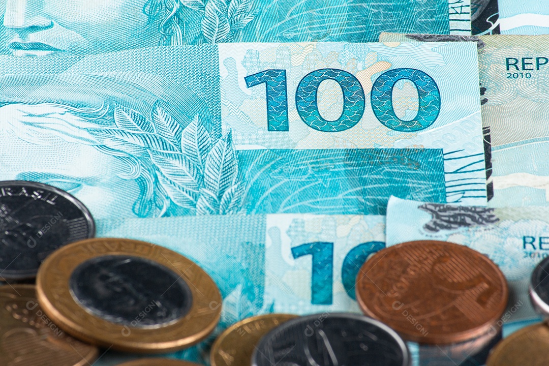 Dinheiro brasileiro com moedas de 1 real espalhadas sobre notas de 100 reais