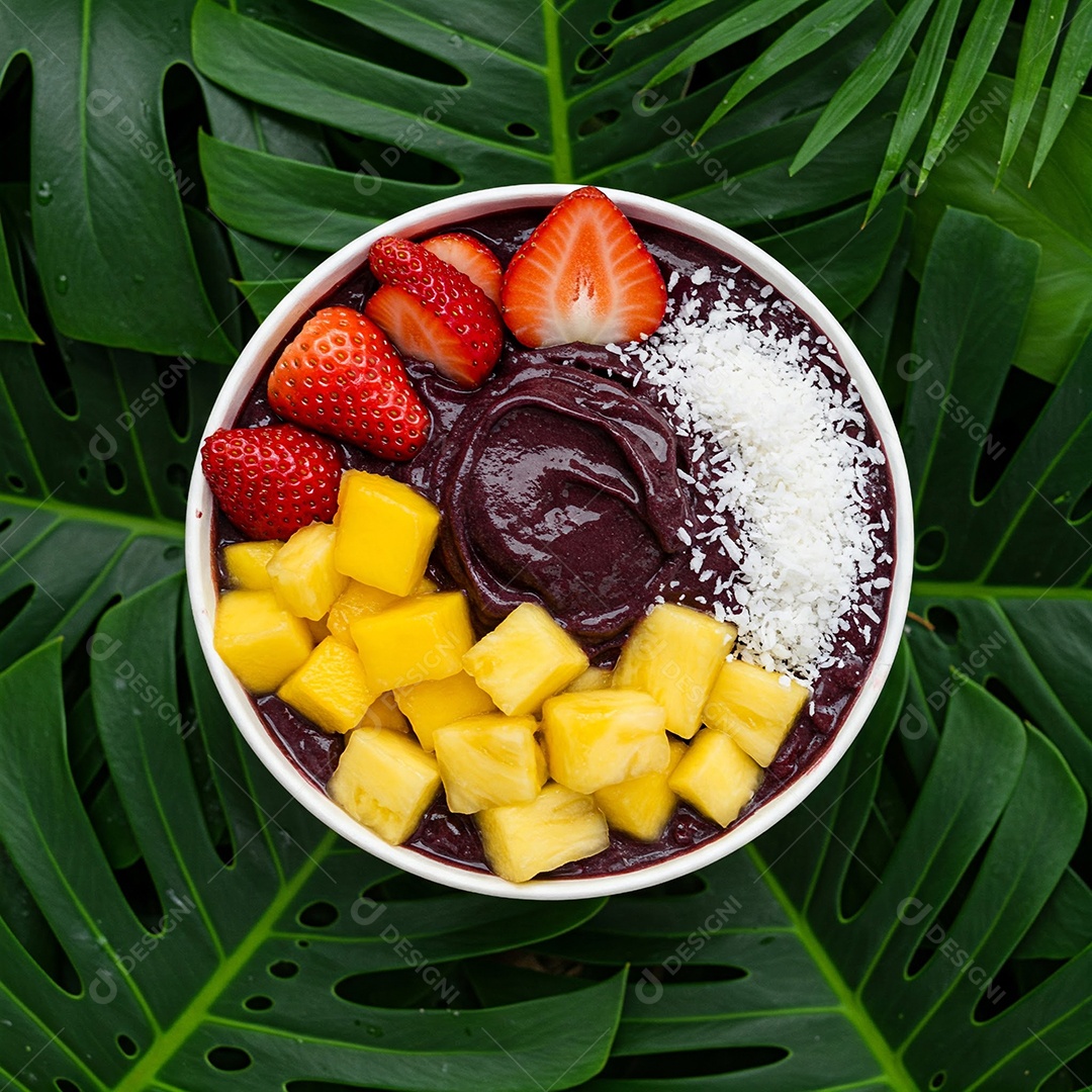 Tigela de açaí colorida com frutas frescas e coco em fundo de folhas tropicais