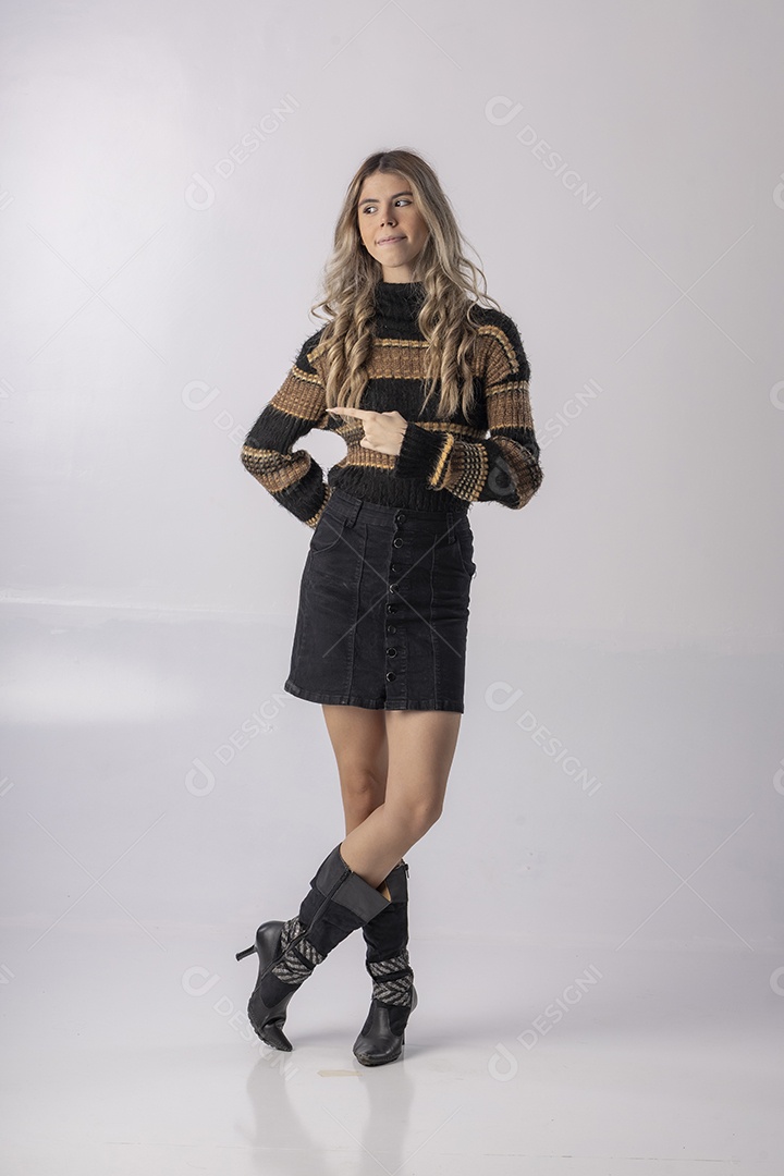 Jovem vestindo blusa e saia apontando para o lado em foto de estúdio