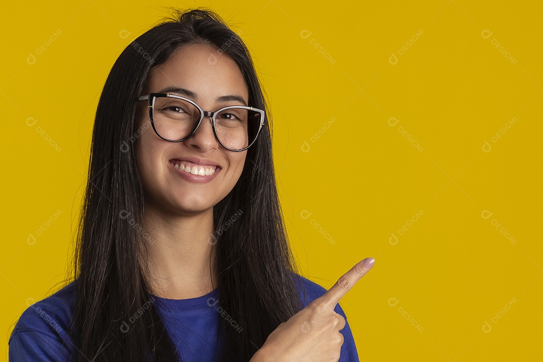 Jovem brasileira usando óculos e camisa azul em um estúdio com fundo amarelo