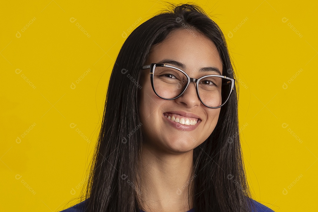Jovem brasileira usando óculos e camisa azul em um estúdio com fundo amarelo