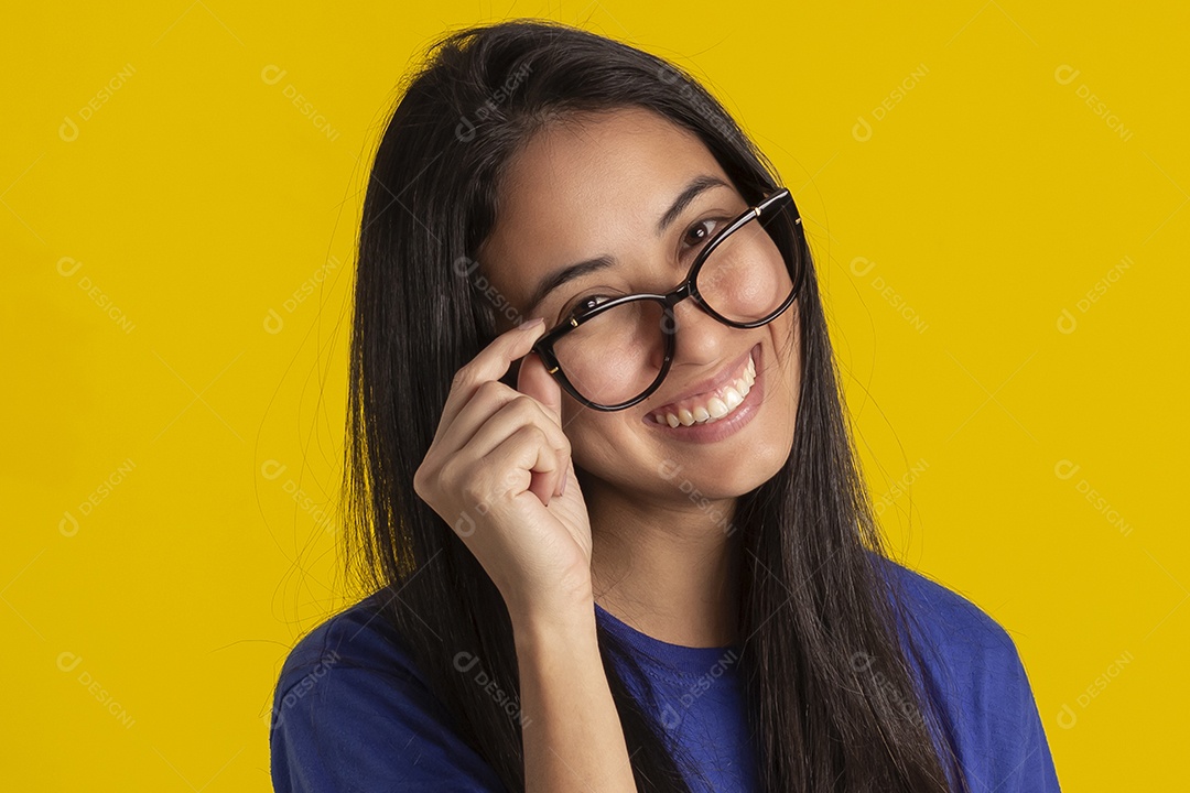 Jovem brasileira usando óculos e camisa azul em um estúdio com fundo amarelo