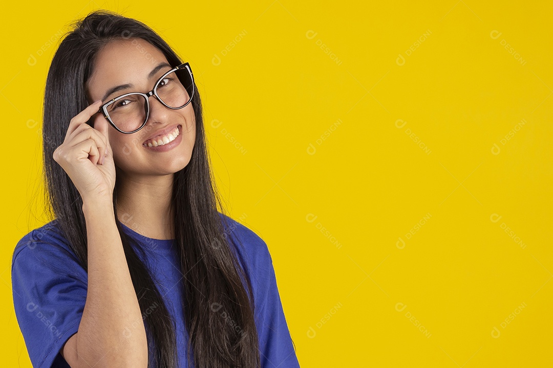 Jovem brasileira usando óculos e camisa azul em um estúdio com fundo amarelo