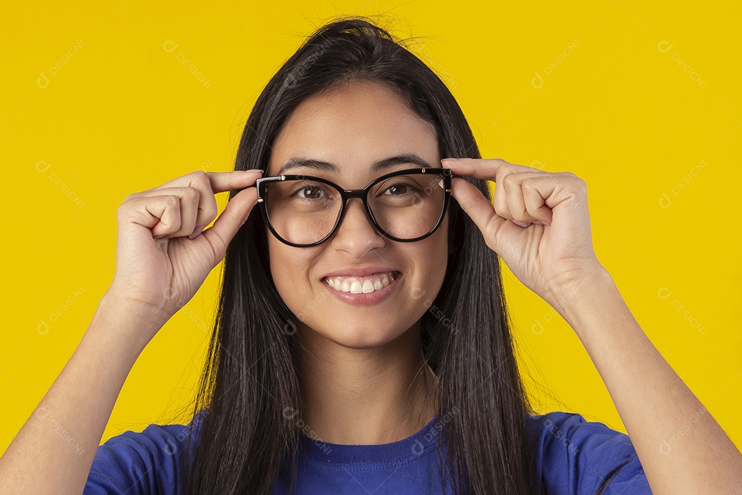Jovem brasileira usando óculos e camisa azul em um estúdio com fundo amarelo