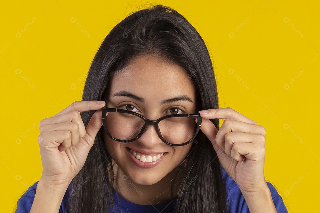 Jovem brasileira usando óculos e camisa azul em um estúdio com fundo amarelo
