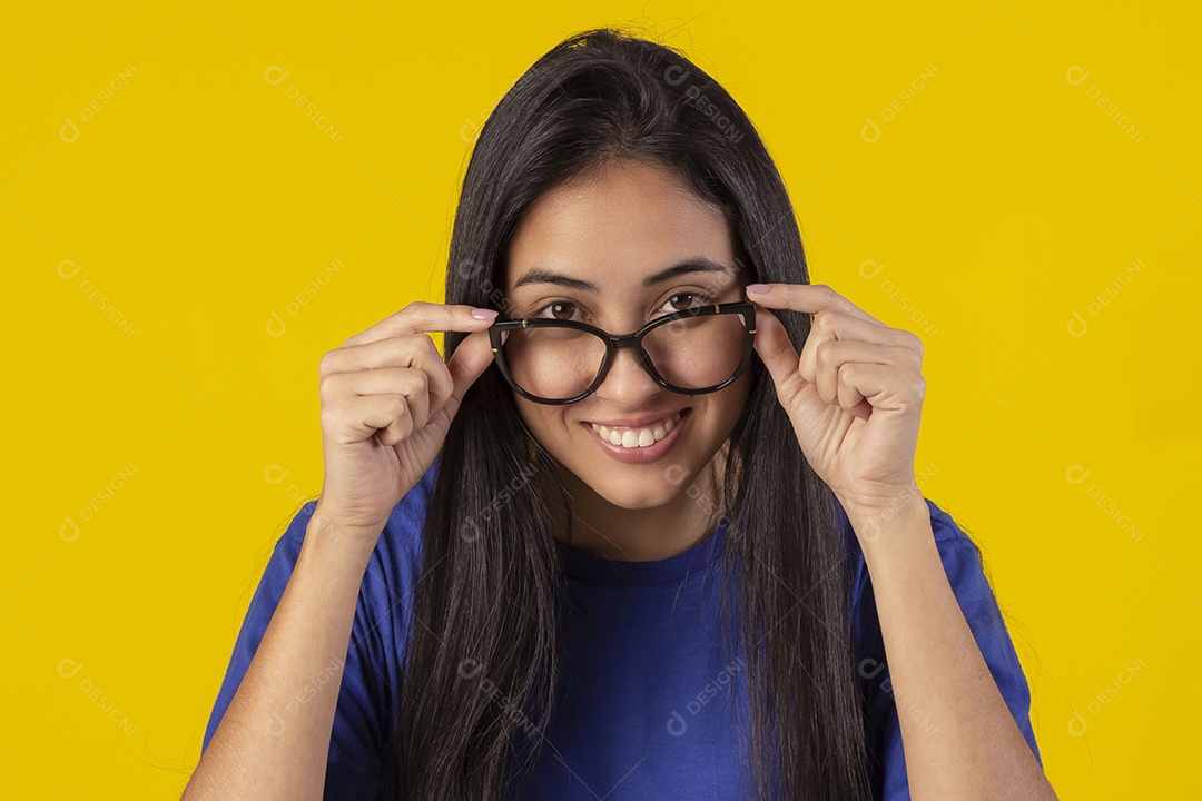Jovem brasileira usando óculos e camisa azul em um estúdio com fundo amarelo