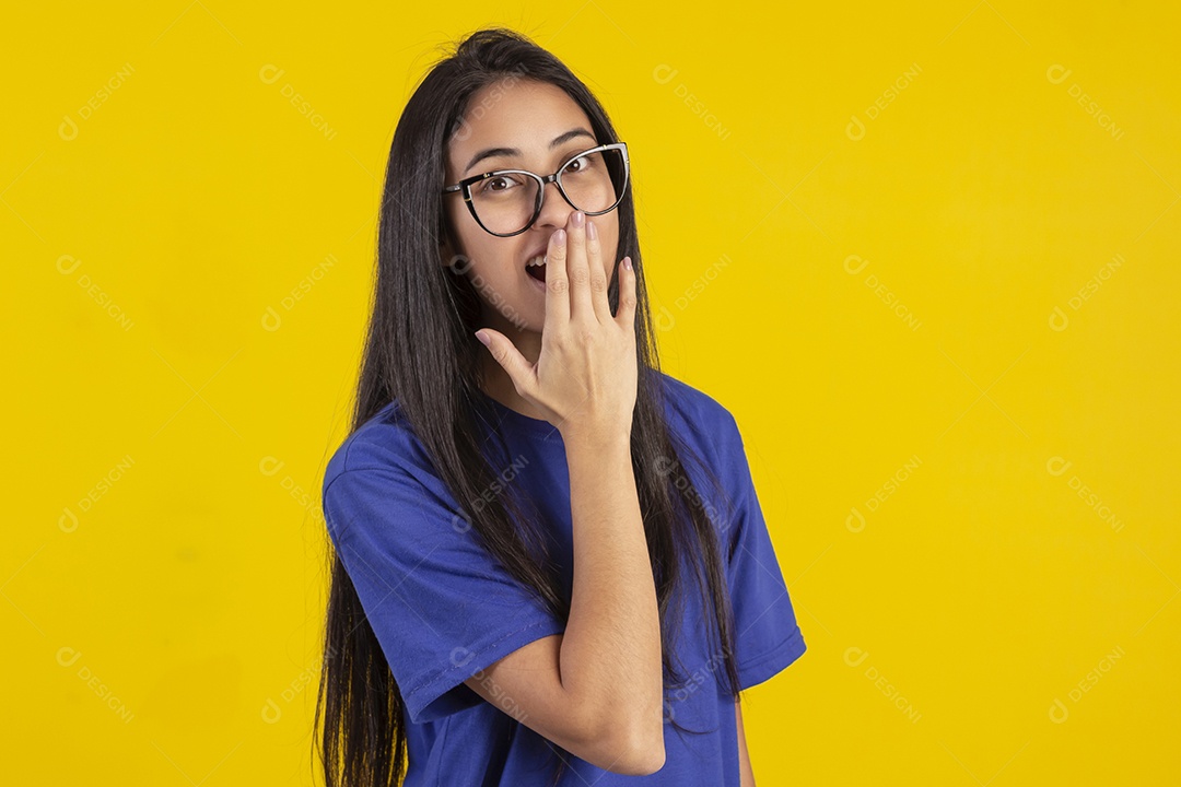 Jovem brasileira usando óculos e camisa azul em um estúdio com fundo amarelo