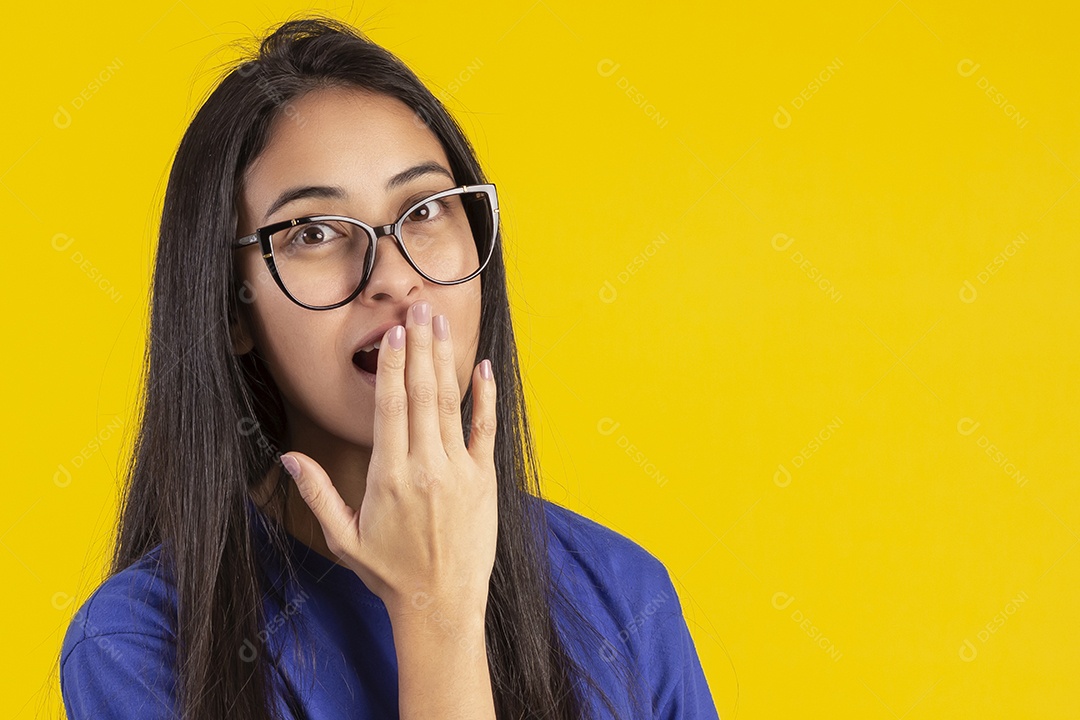 Jovem brasileira usando óculos e camisa azul em um estúdio com fundo amarelo
