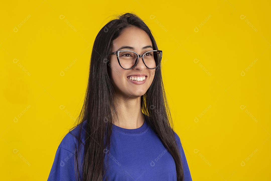 Jovem brasileira usando óculos e camisa azul em um estúdio com fundo amarelo