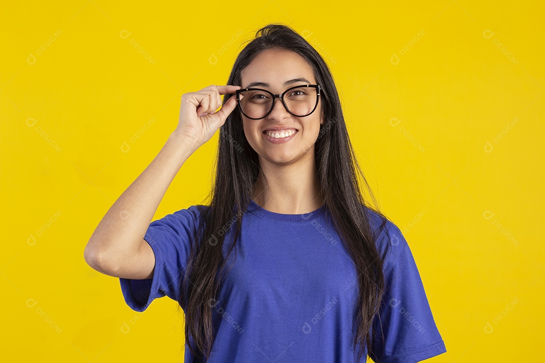 Jovem brasileira usando óculos e camisa azul em um estúdio com fundo amarelo