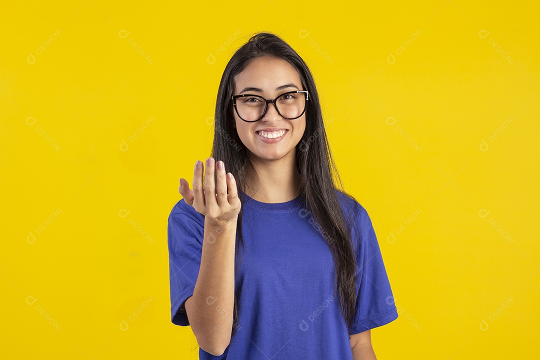 Jovem brasileira usando óculos e camisa azul em um estúdio com fundo amarelo