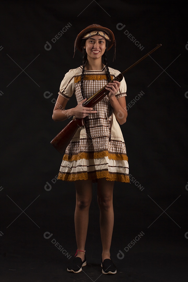 Jovem bonita com trajes de festa junina usando vestido chapéu e com uma espingarda