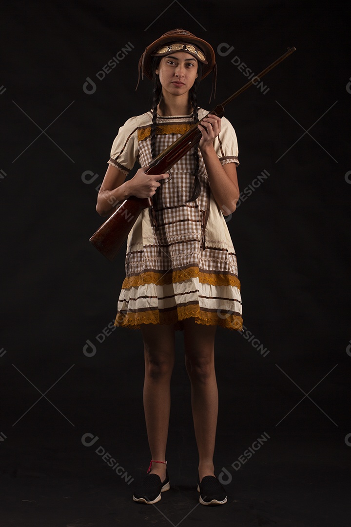 Jovem bonita com trajes de festa junina usando vestido chapéu e com uma espingarda