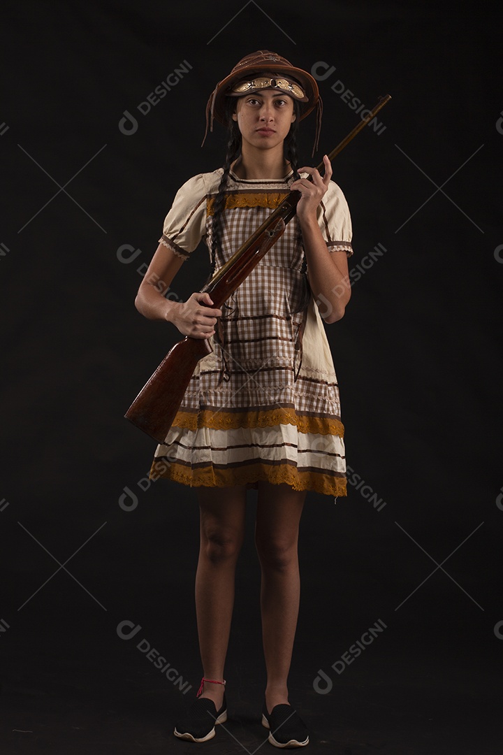 Jovem bonita com trajes de festa junina usando vestido chapéu e com uma espingarda