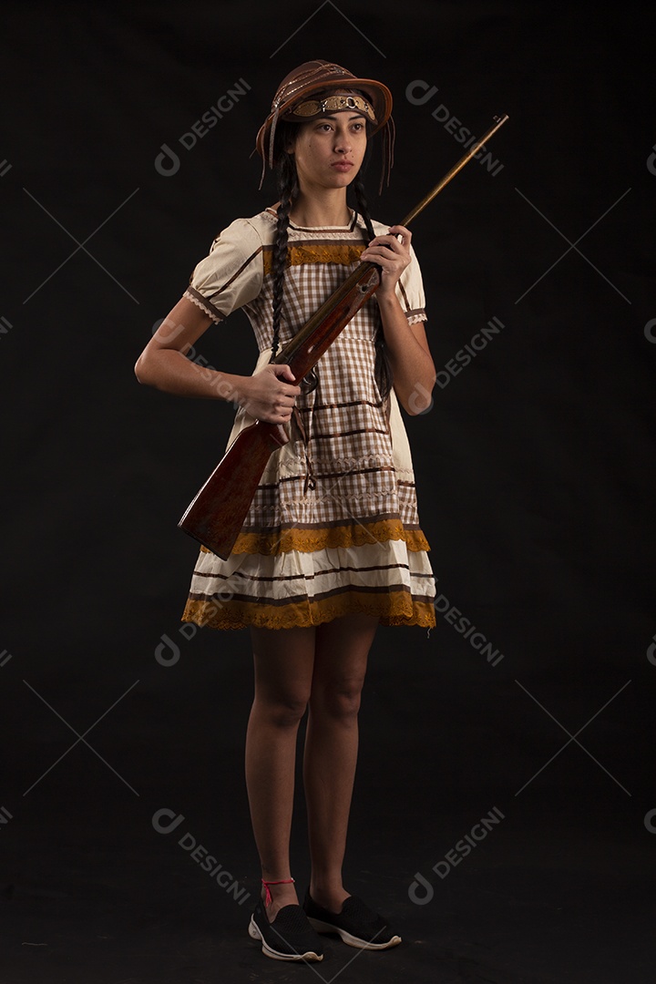 Jovem bonita com trajes de festa junina usando vestido chapéu e com uma espingarda