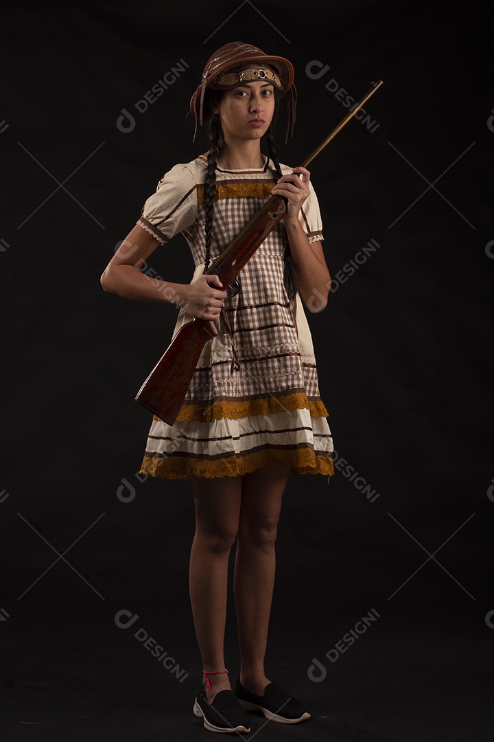 Jovem bonita com trajes de festa junina usando vestido chapéu e com uma espingarda