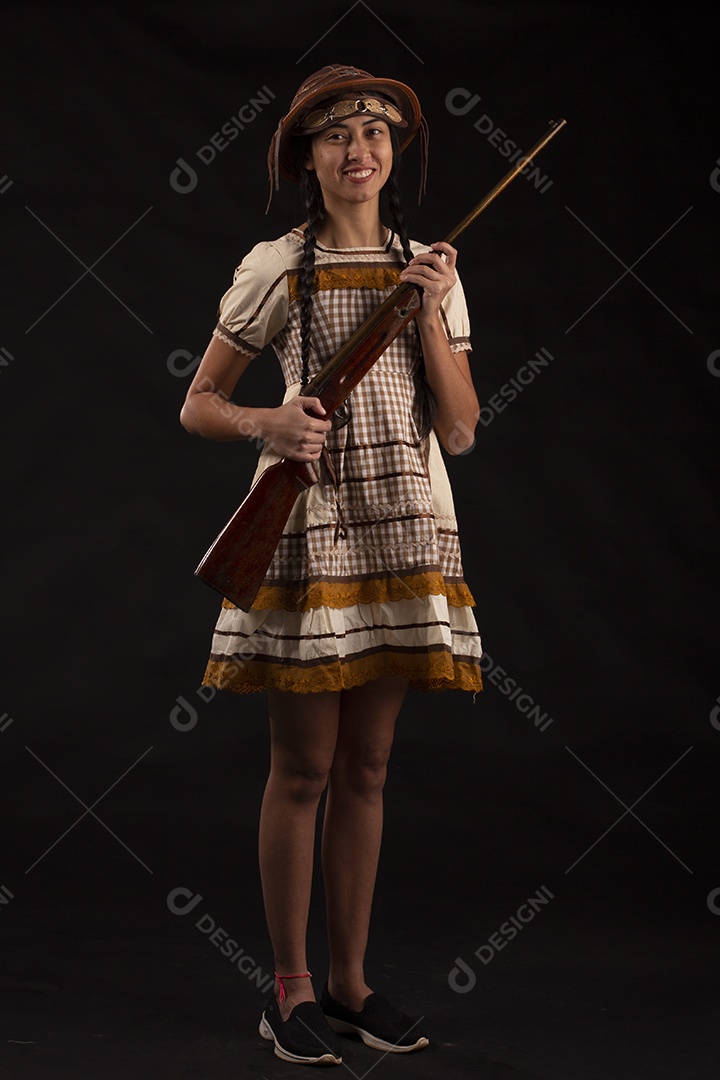 Jovem bonita com trajes de festa junina usando vestido chapéu e com uma espingarda