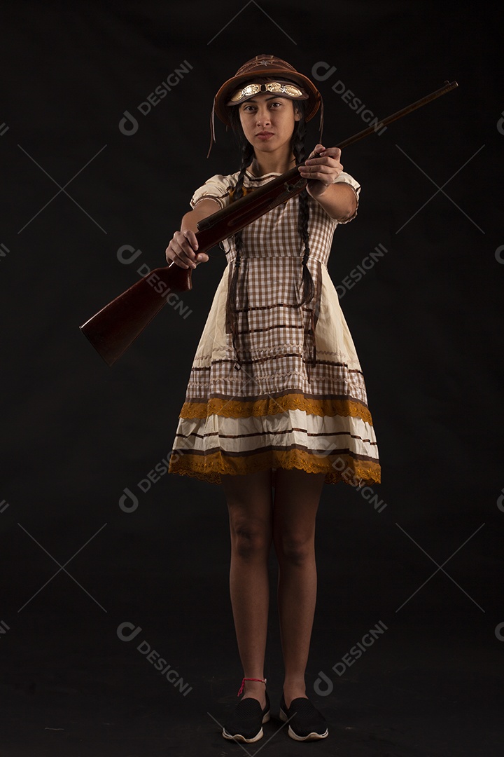 Jovem bonita com trajes de festa junina usando vestido chapéu e com uma espingarda