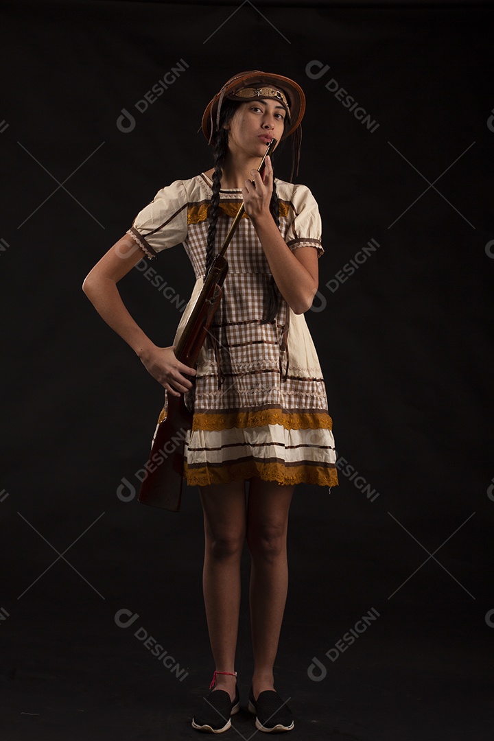 Jovem bonita com trajes de festa junina usando vestido chapéu e com uma espingarda