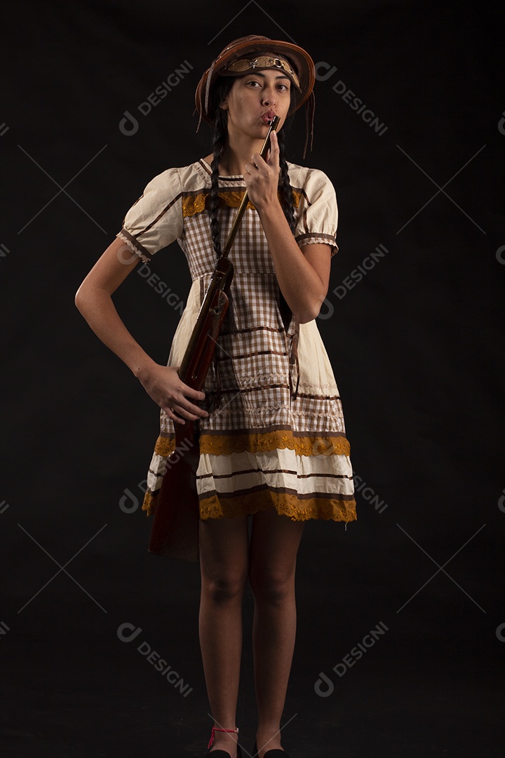 Jovem bonita com trajes de festa junina usando vestido chapéu e com uma espingarda