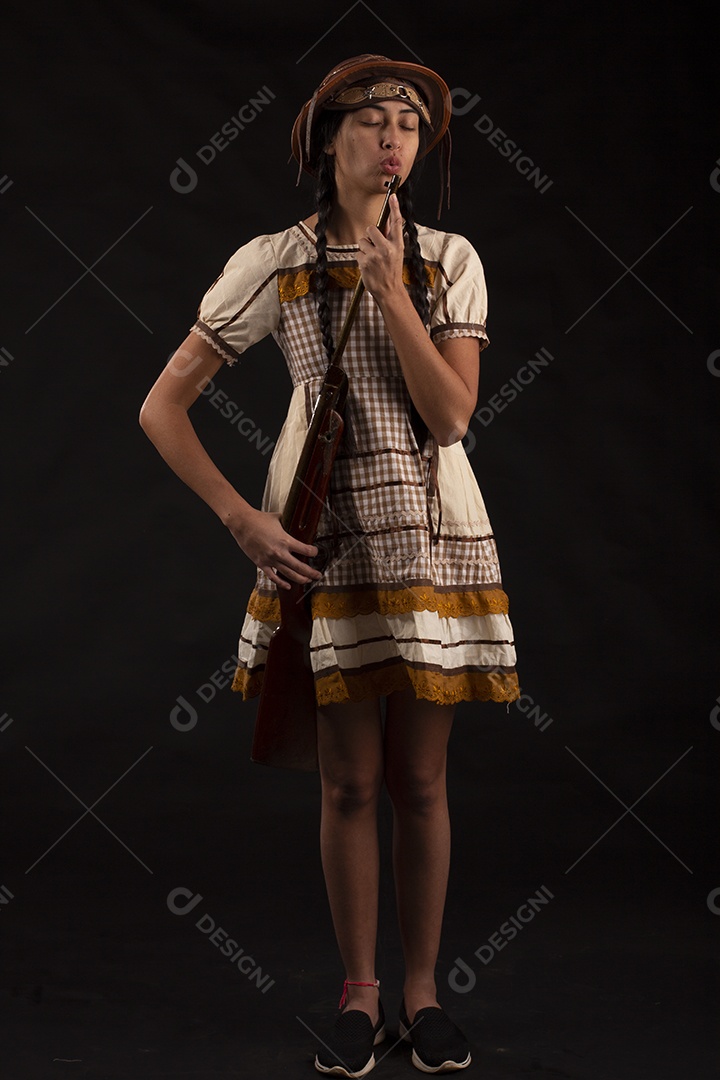 Jovem bonita com trajes de festa junina usando vestido chapéu e com uma espingarda