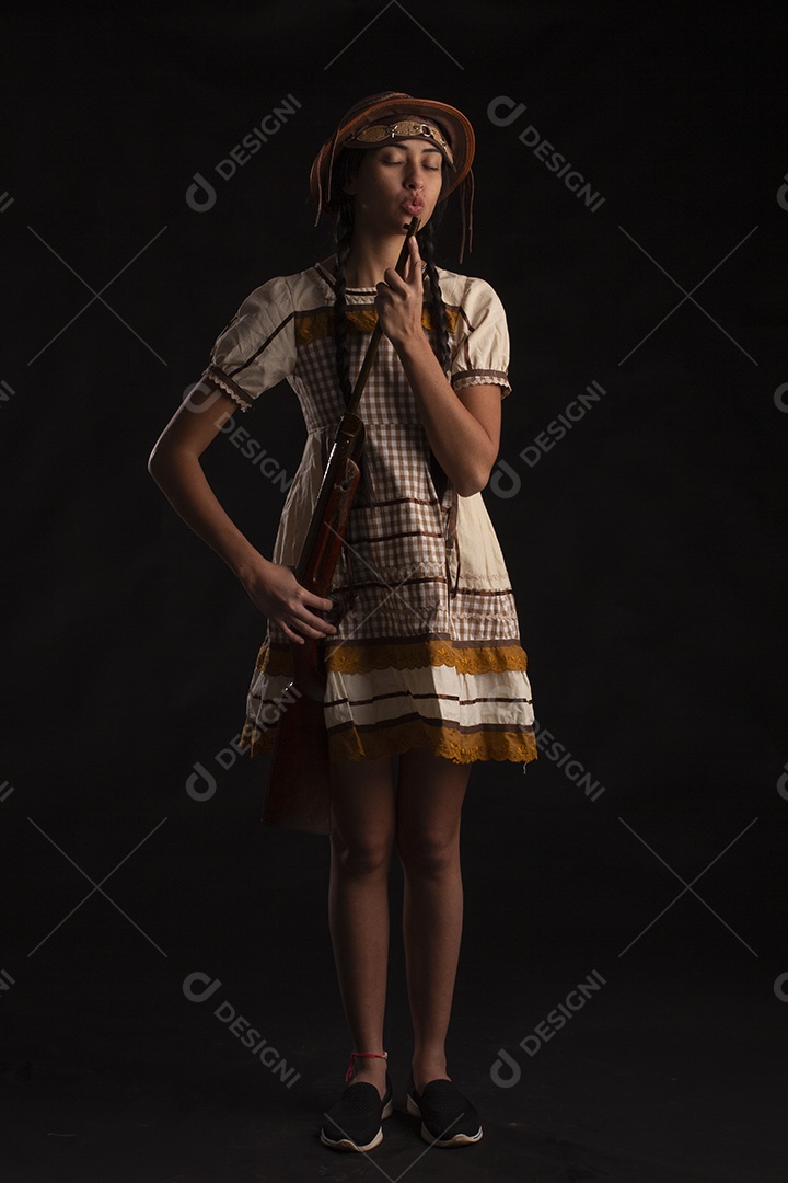 Jovem bonita com trajes de festa junina usando vestido chapéu e com uma espingarda