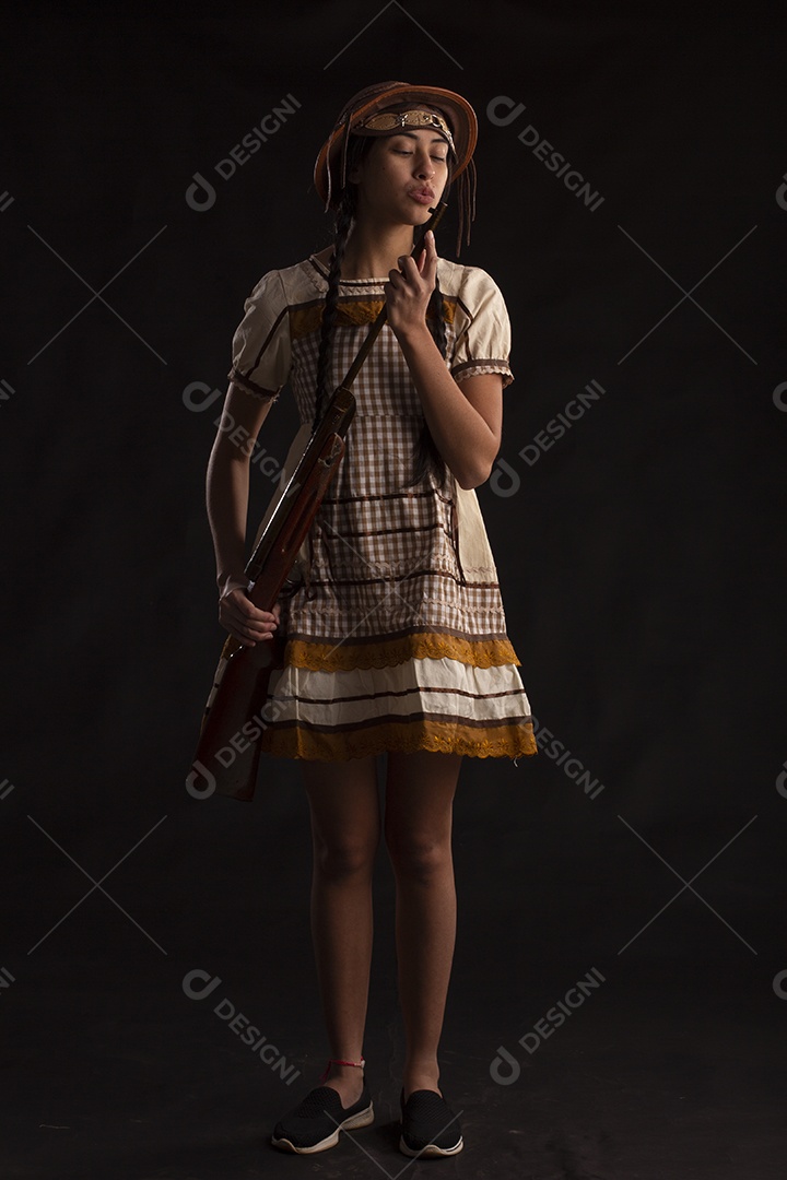 Jovem bonita com trajes de festa junina usando vestido chapéu e com uma espingarda