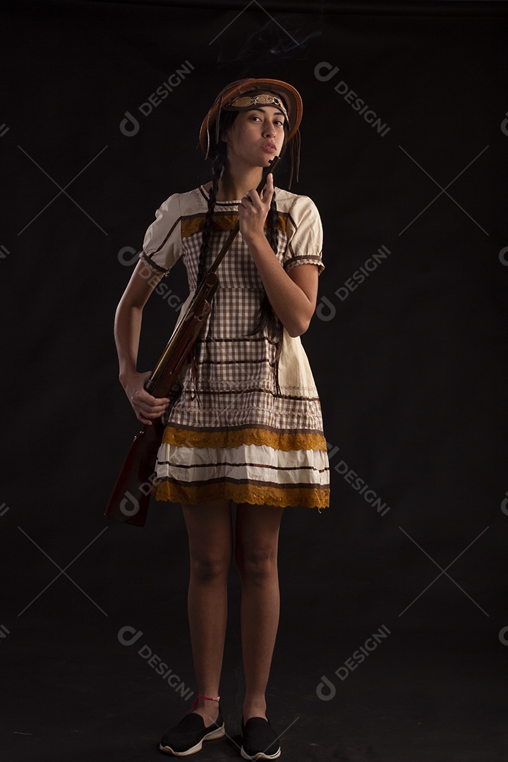 Jovem bonita com trajes de festa junina usando vestido chapéu e com uma espingarda