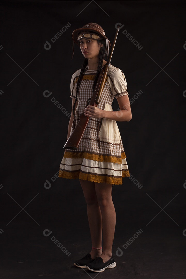 Jovem com trajes típico de festa junina vestido chapéu de couro segurando espingarda