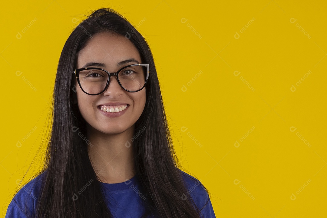 Jovem brasileira usando óculos e camisa azul em um estúdio com fundo amarelo