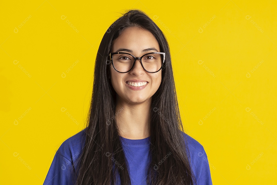 Jovem brasileira usando óculos e camisa azul em um estúdio com fundo amarelo