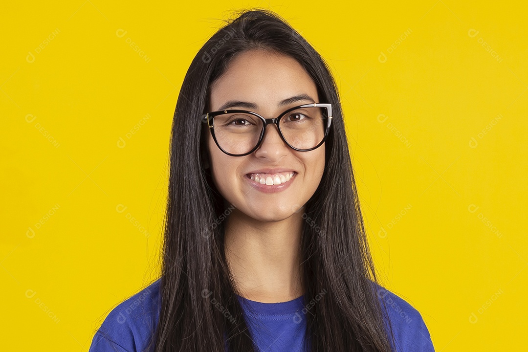 Jovem brasileira usando óculos e camisa azul em um estúdio com fundo amarelo