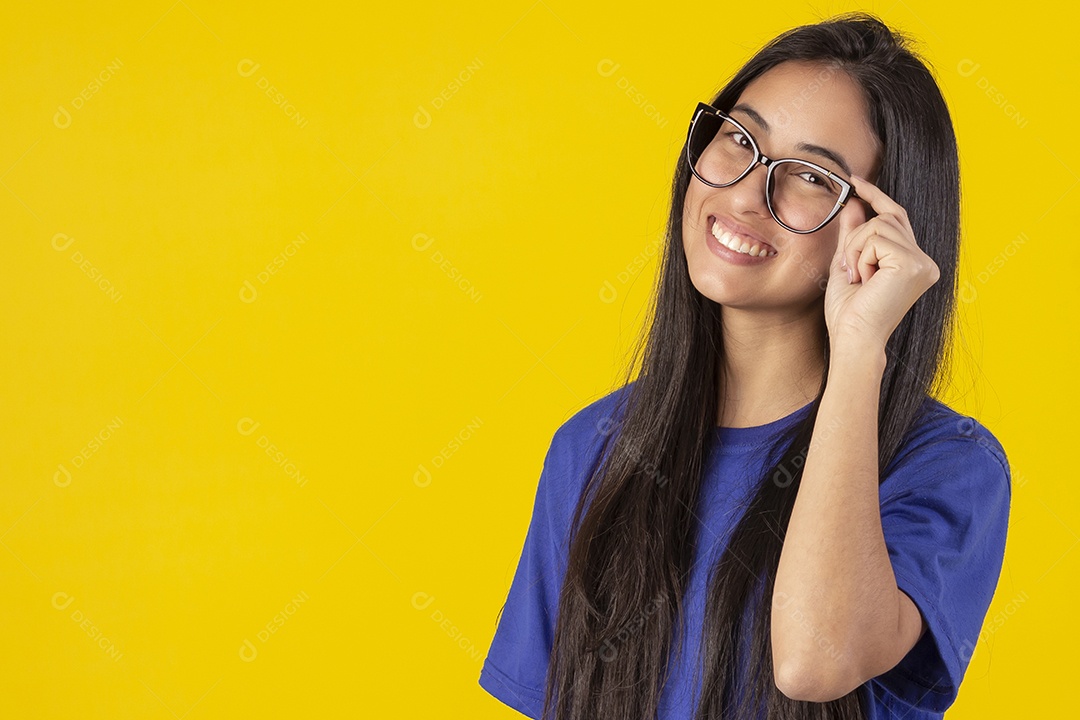 Jovem brasileira usando óculos e camisa azul em um estúdio com fundo amarelo