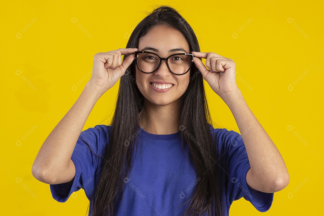 Jovem brasileira usando óculos e camisa azul em um estúdio com fundo amarelo