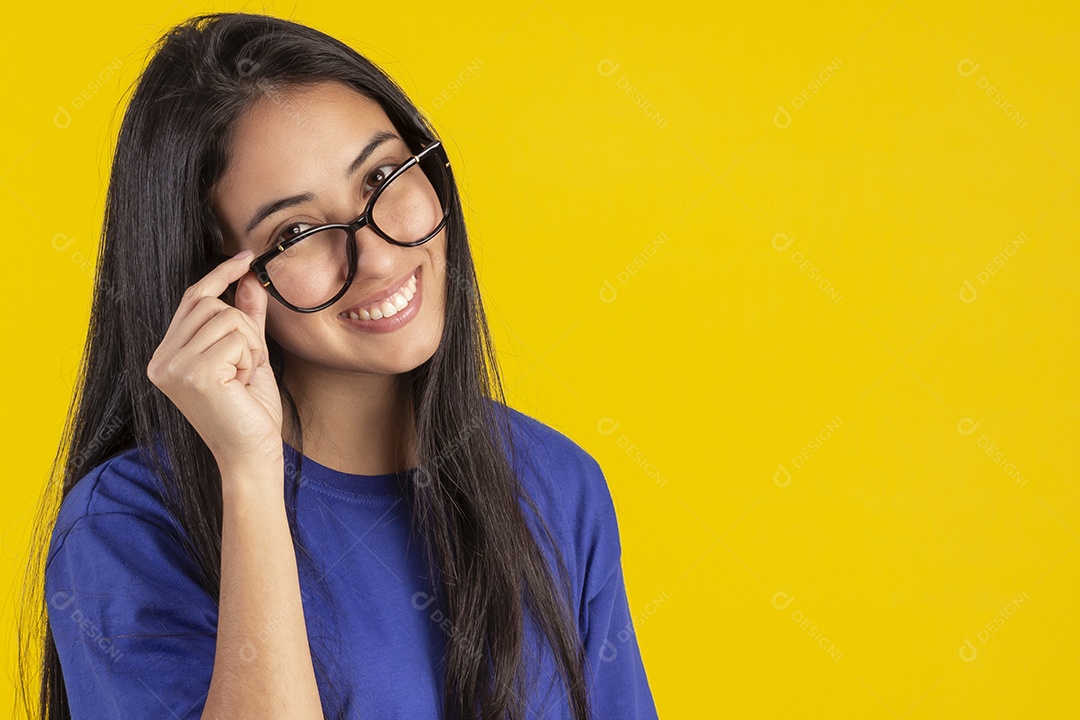 Jovem brasileira usando óculos e camisa azul em um estúdio com fundo amarelo