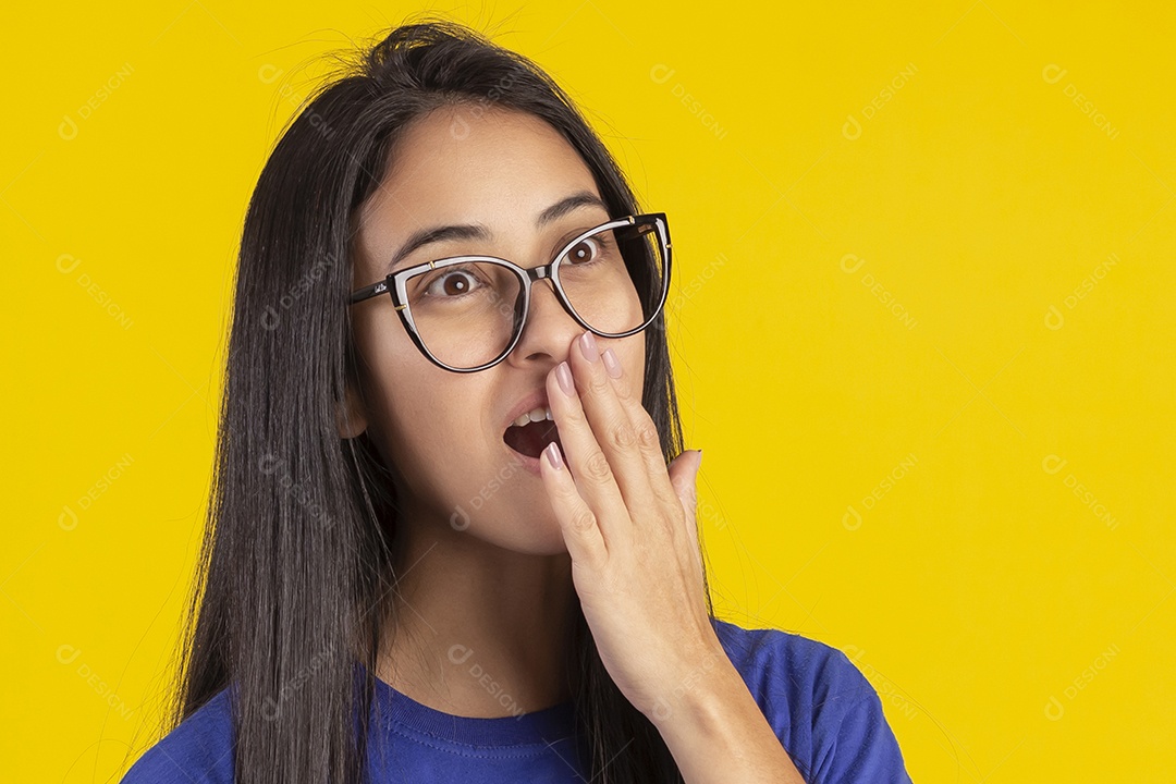 Jovem brasileira usando óculos e camisa azul em um estúdio com fundo amarelo