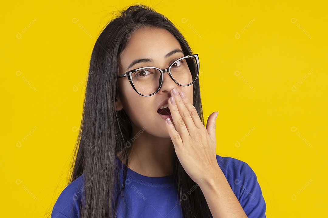 Jovem brasileira usando óculos e camisa azul em um estúdio com fundo amarelo