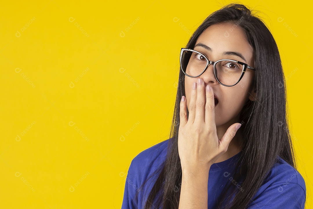 Jovem brasileira usando óculos e camisa azul em um estúdio com fundo amarelo