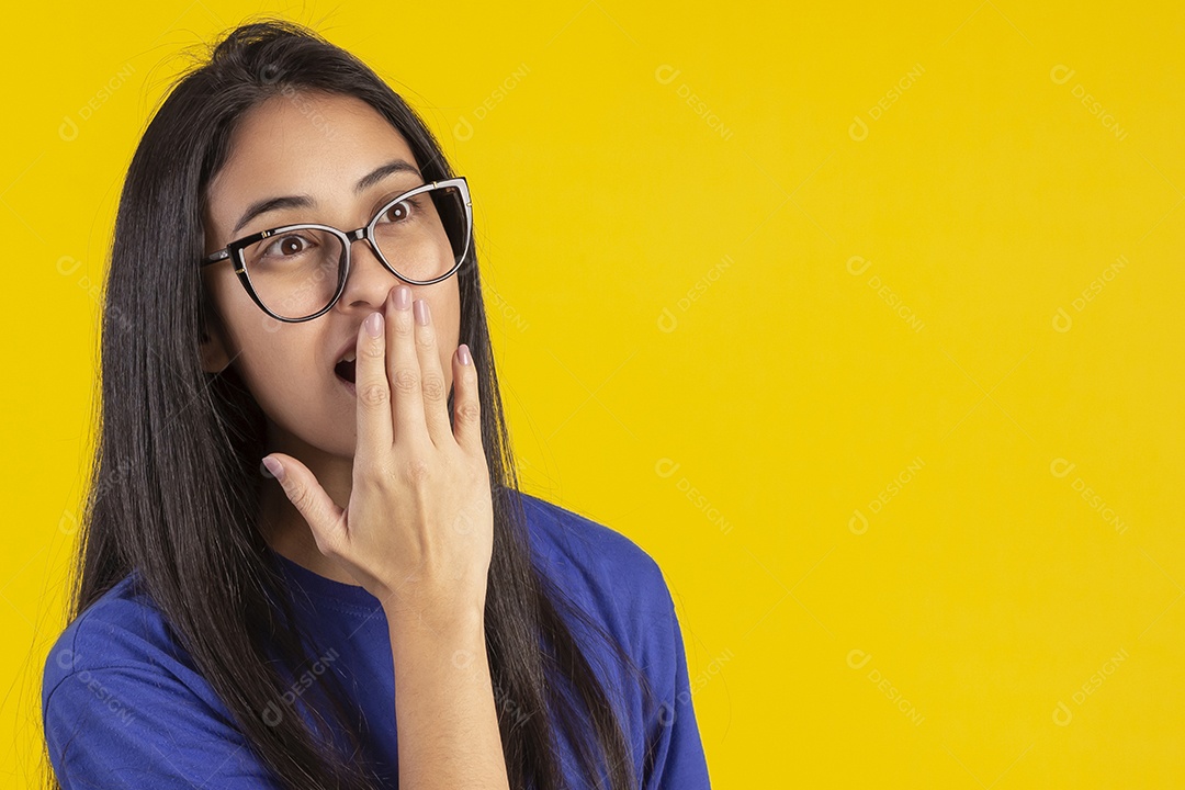 Jovem brasileira usando óculos e camisa azul em um estúdio com fundo amarelo