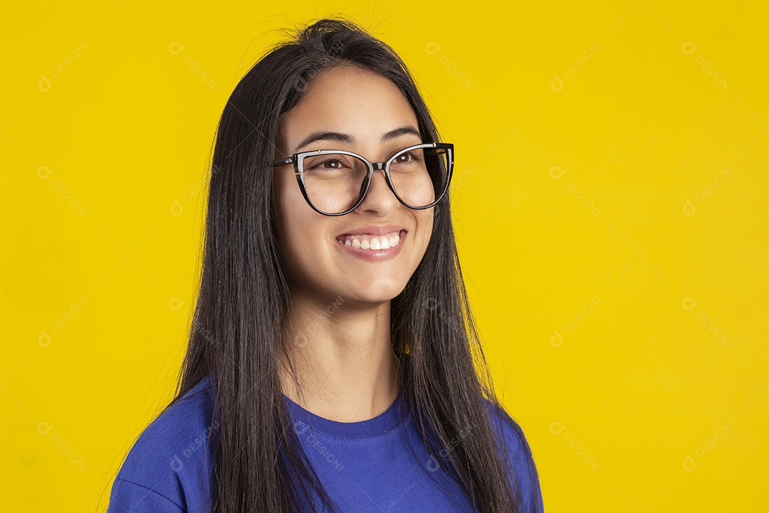 Jovem brasileira usando óculos e camisa azul em um estúdio com fundo amarelo