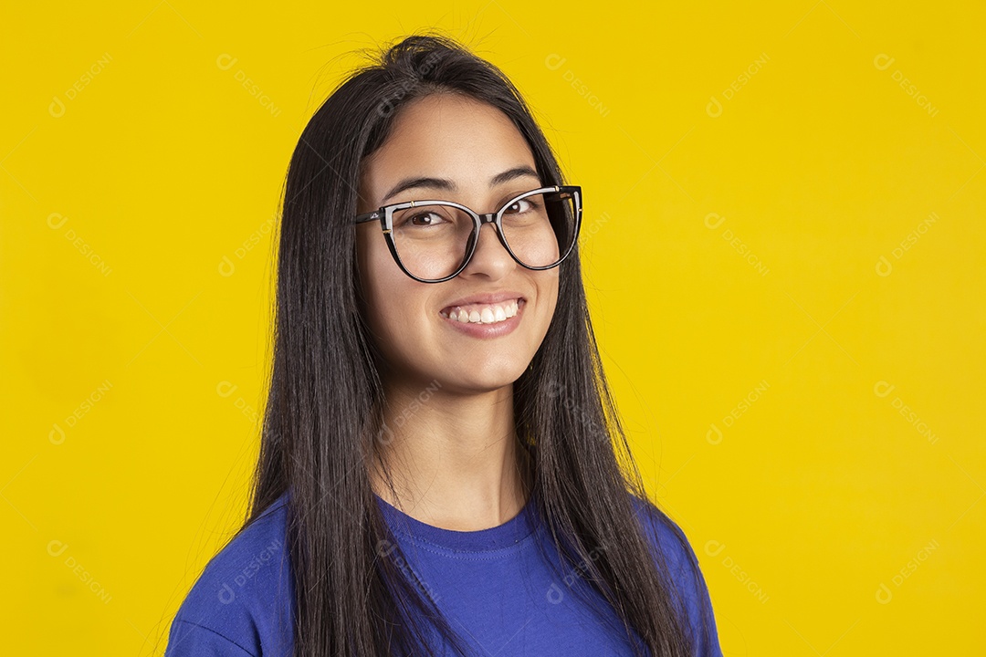 Jovem brasileira usando óculos e camisa azul em um estúdio com fundo amarelo