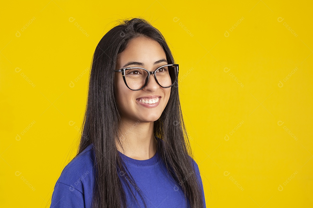 Jovem brasileira usando óculos e camisa azul em um estúdio com fundo amarelo