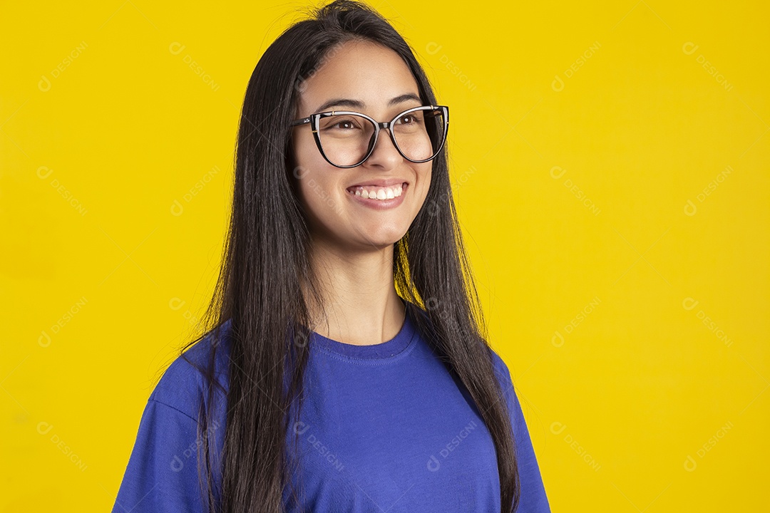 Jovem brasileira usando óculos e camisa azul em um estúdio com fundo amarelo