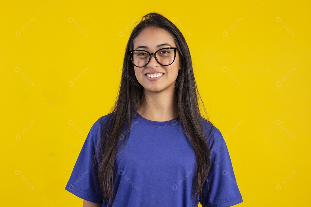 Jovem brasileira usando óculos e camisa azul em um estúdio com fundo amarelo