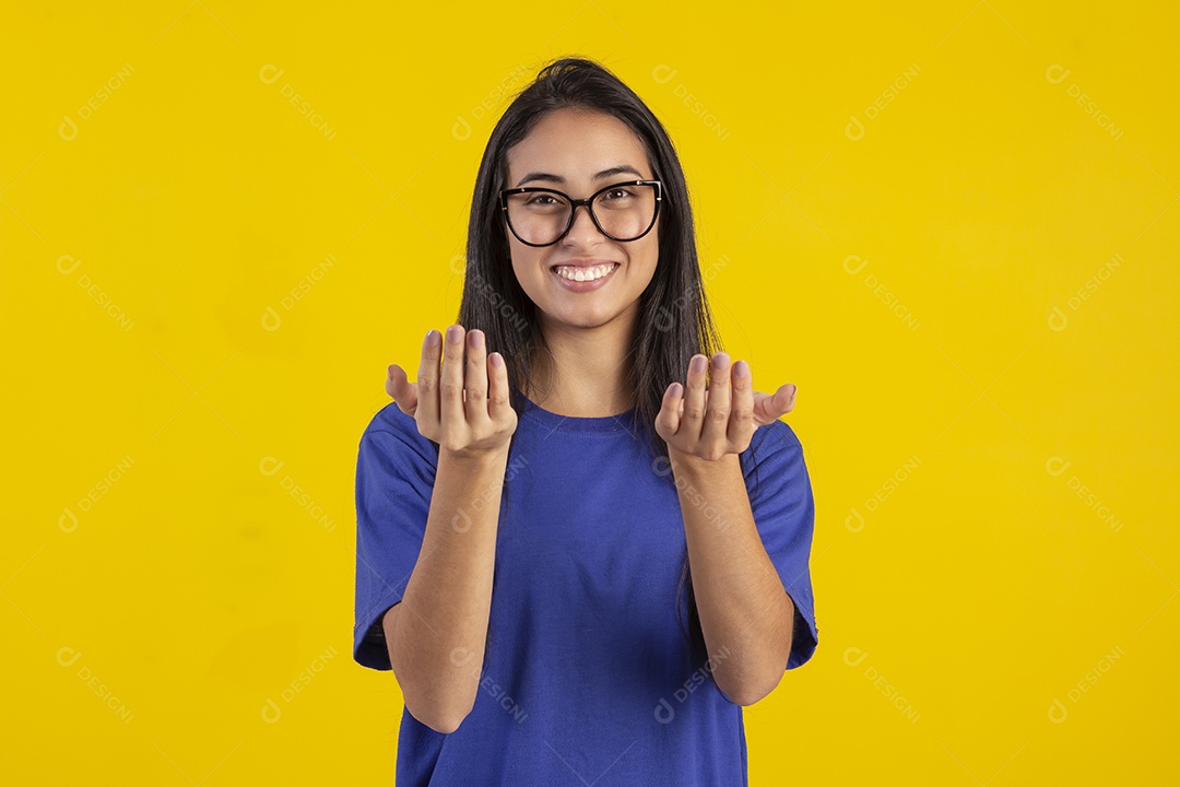 Jovem brasileira usando óculos e camisa azul em um estúdio com fundo amarelo