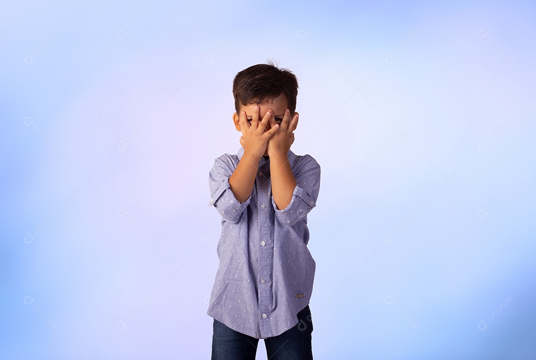 Criança do sexo masculino em foto de estúdio com fundo azul vestindo camisa e jeans
