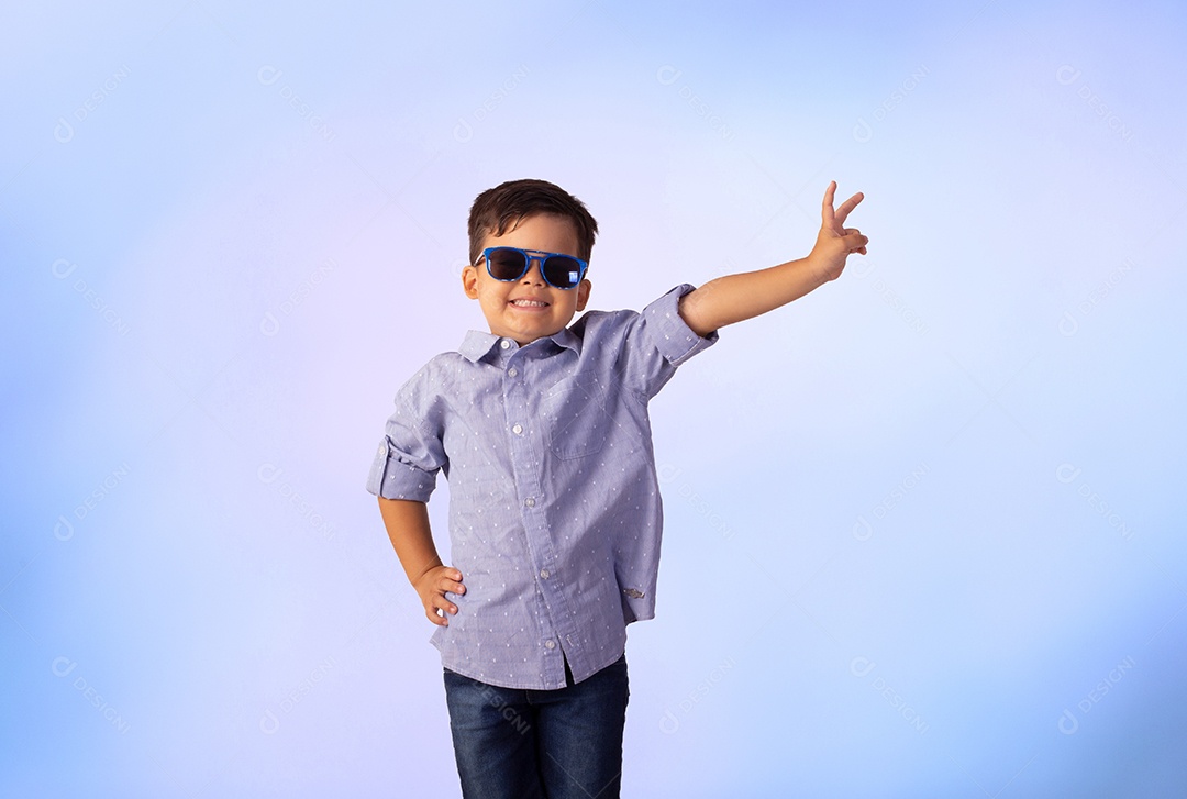 Criança do sexo masculino em foto de estúdio com fundo azul vestindo camisa e jeans