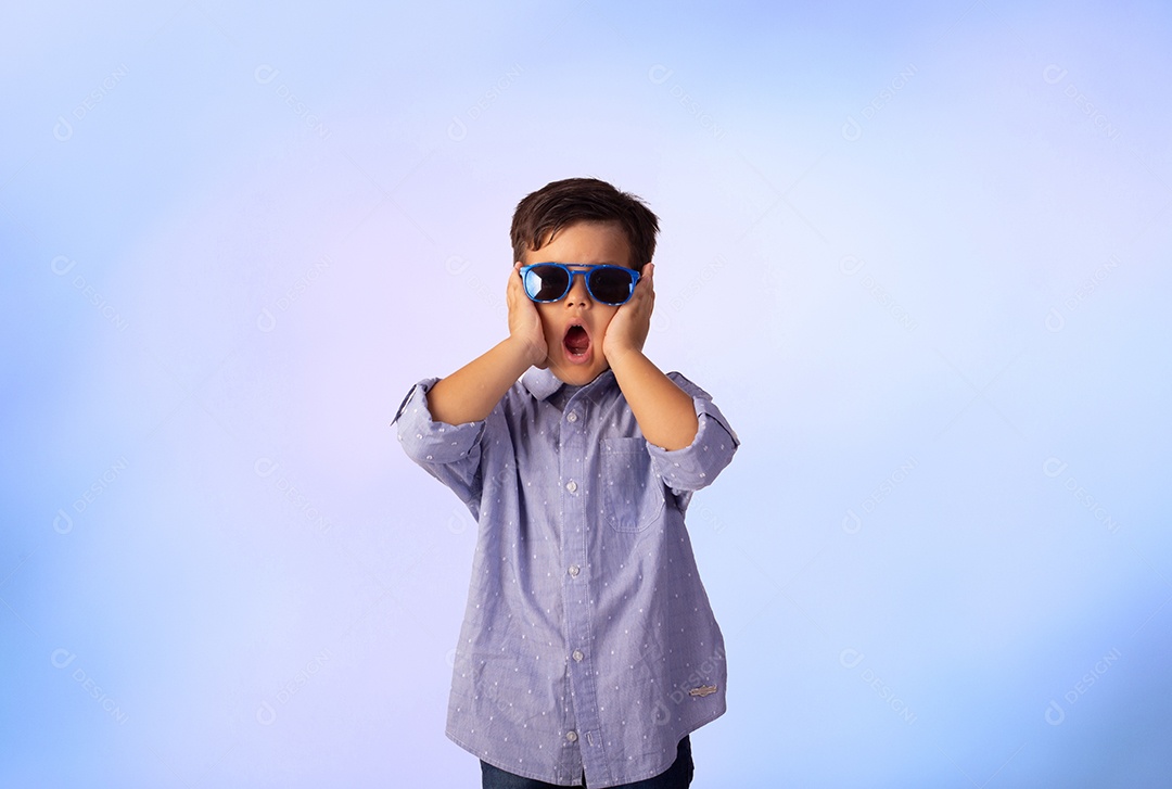 Criança do sexo masculino em foto de estúdio com fundo azul vestindo camisa e jeans